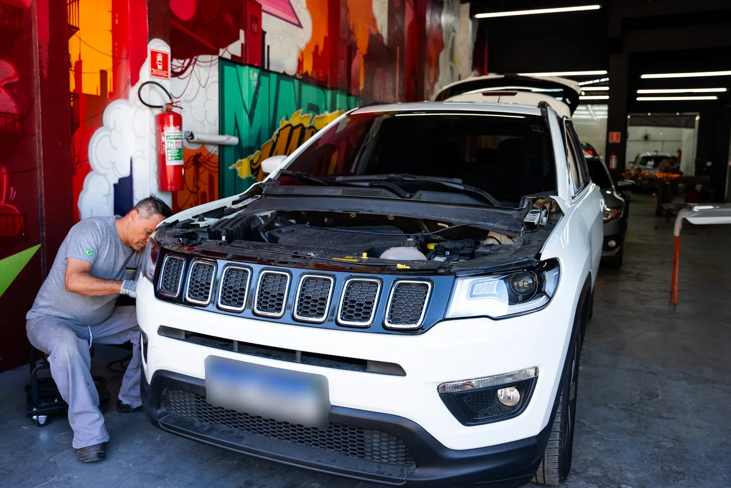Profissional reparando um carro branco desmontado em oficina de funilaria e pintura em Arujá