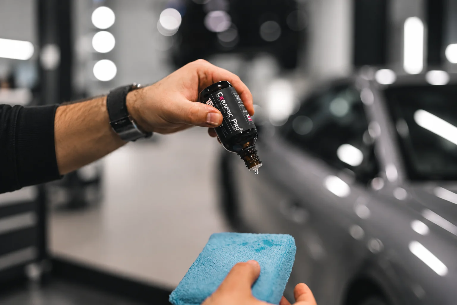 Mãos preparando um aplicador azul com revestimento cerâmico ao lado de um carro cinza
