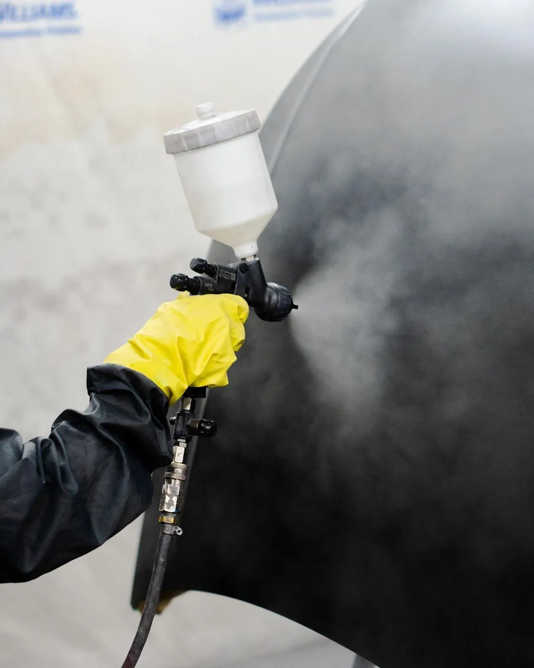Profissional aplica tinta automotiva com pistola de pintura na cabine